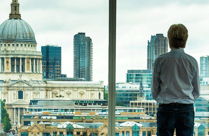A person looks out a window at a cityscape with St. Paul's Cathedral in the background.