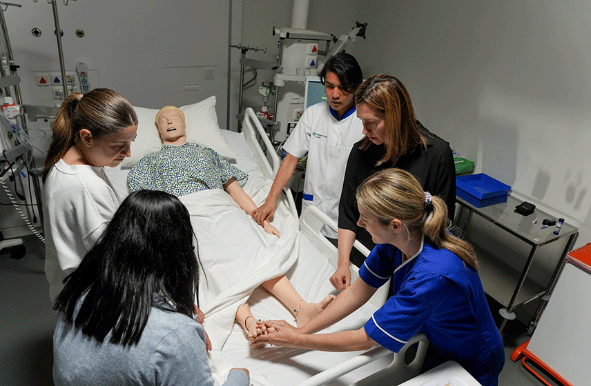 Medical team practicing patient care on a mannequin in a hospital bed.