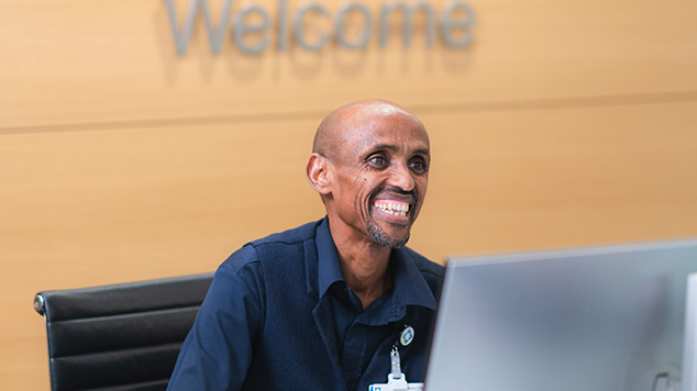 Greeter sitting at a desk in front of a "Welcome" sign.