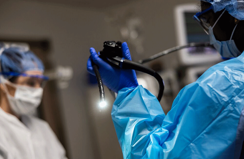 Medical staff in protective gear readies an endoscope for a procedure.