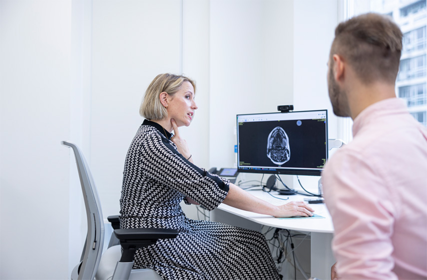 A Cleveland Clinic London caregiver pointing at her throat while showing someone an X-ray of a skull