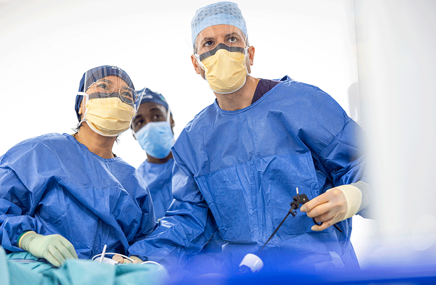 Three surgeons in blue surgical gowns and face masks performing a procedure in an operating room.