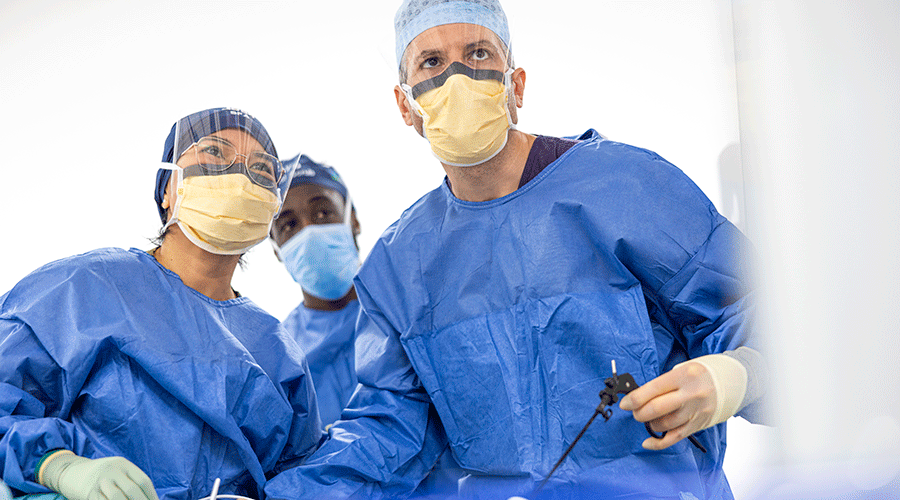 Three surgeons in blue surgical gowns and face masks performing a procedure in an operating room.