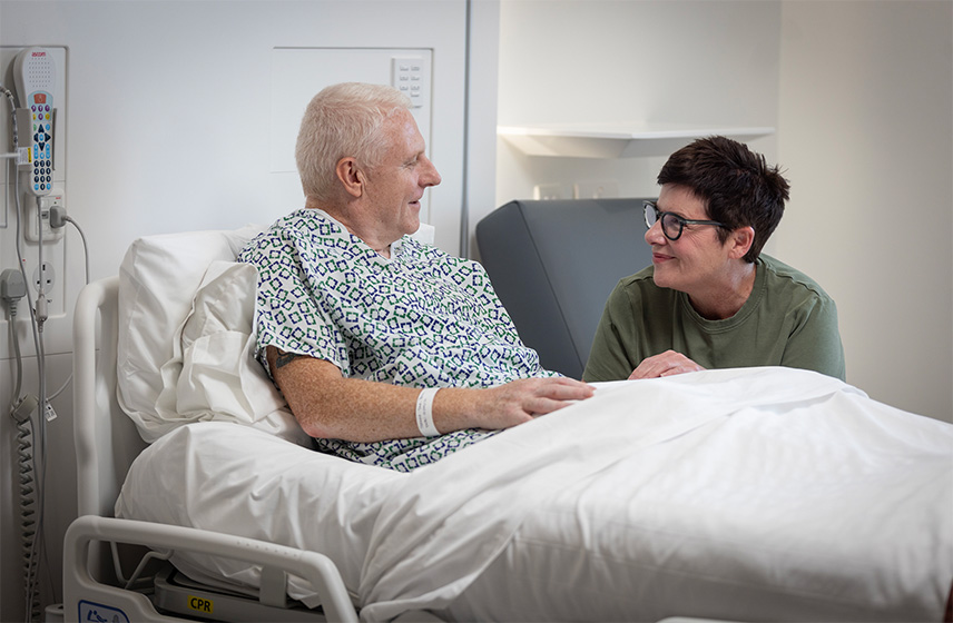 A patient sitting in bed talking to a visitor.