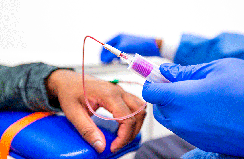 Syringe, attached to a tube, administering medication into a patients' hand.