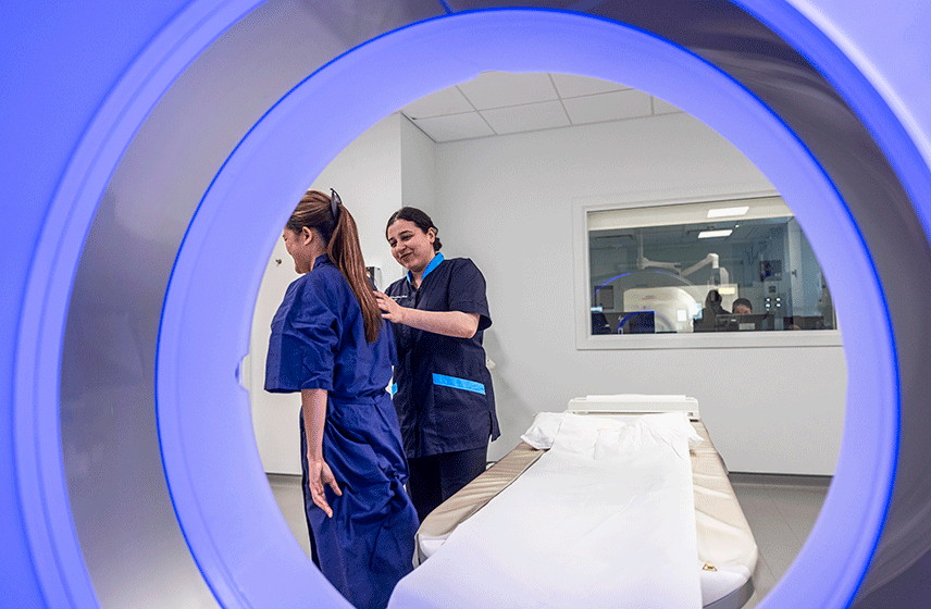 Nurse helping patient lie down for an MRI scan in a medical room.