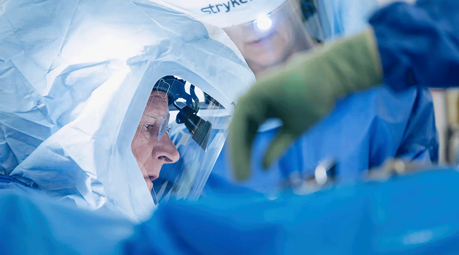 Surgeon performing a procedure using robotic-assisted equipment in a sterile operating room.