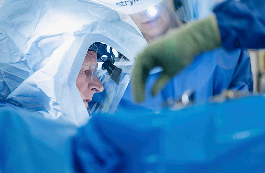 Surgeon performing a procedure using robotic-assisted equipment in a sterile operating room.