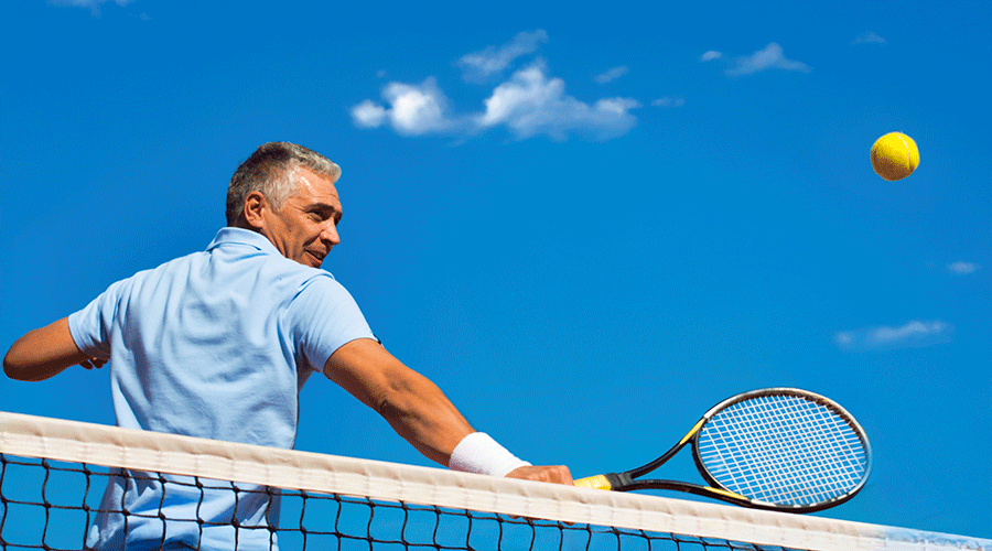 Tennis player hitting a ball over the net on a sunny day with a clear blue sky.