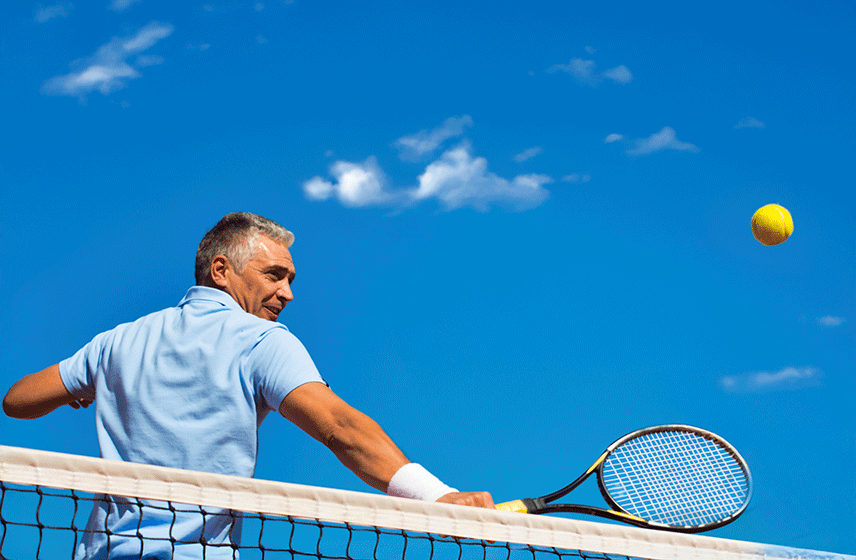 Tennis player hitting a ball over the net on a sunny day with a clear blue sky.
