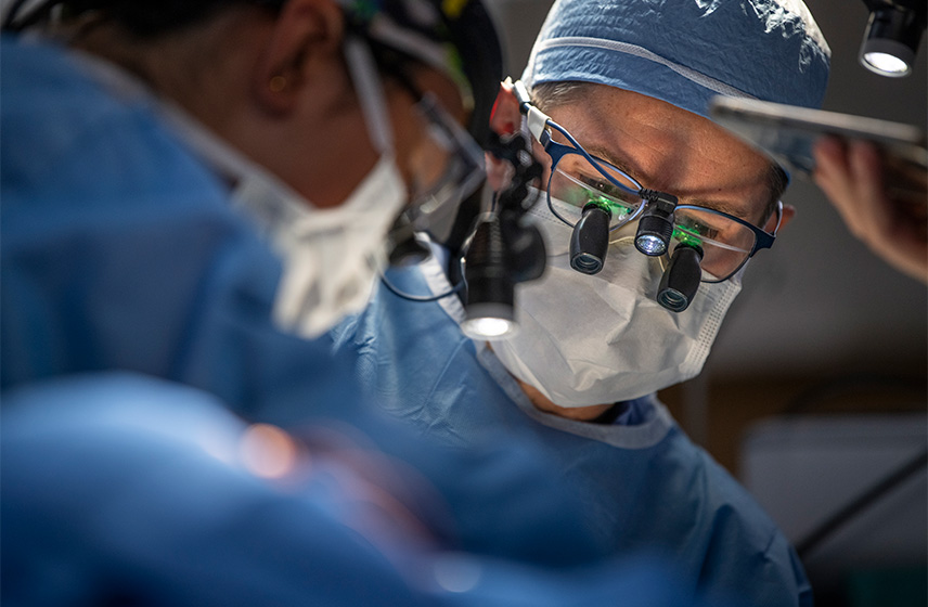 A doctor in scrubs and a face mask performing surgery.