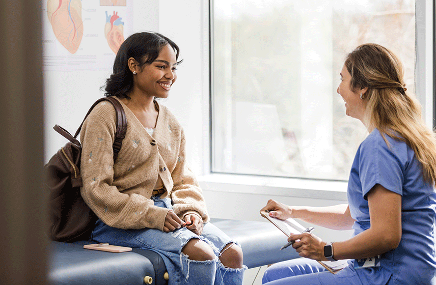 Caregiver talks with a young patient during an appointment in a clinical exam room.